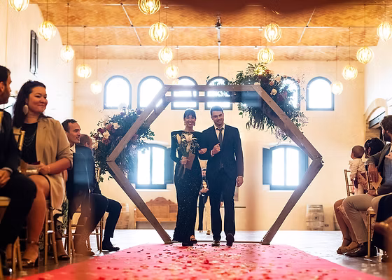 Parella de casats sota un arc de cerimònia geomètric amb convidats celebrant.