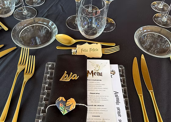 Menú de casament personalitzat amb papereria negra i daurada en un cobert decorat.