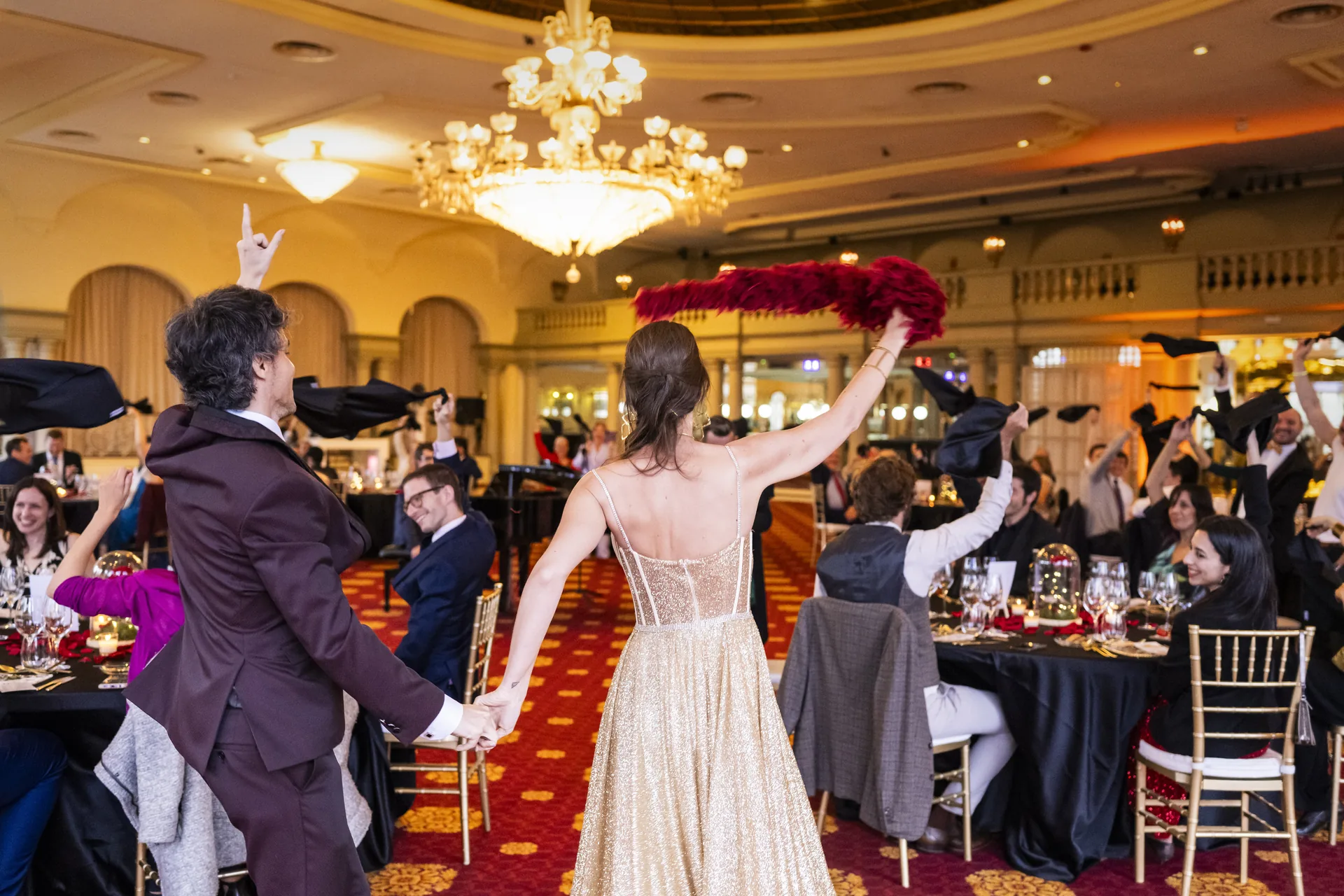 Una parella s’agafa de la mà durant el banquet de casament mentre els convidats agiten tovallons
